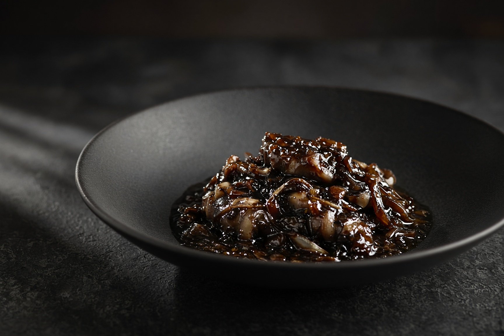 Cuttlefish slow-cooked with onion in its own ink, glossy and near black, on a matt black plate — illustrative AI-generated demo image.